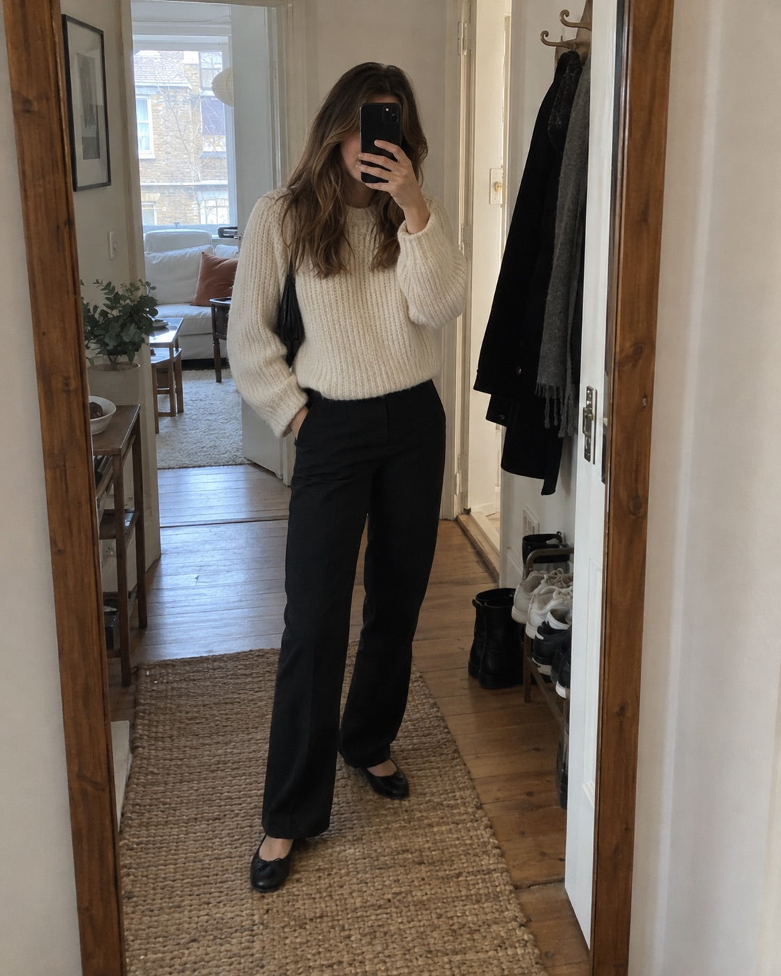 Woman wearing a cream knit and black trousers in a mirror selfie