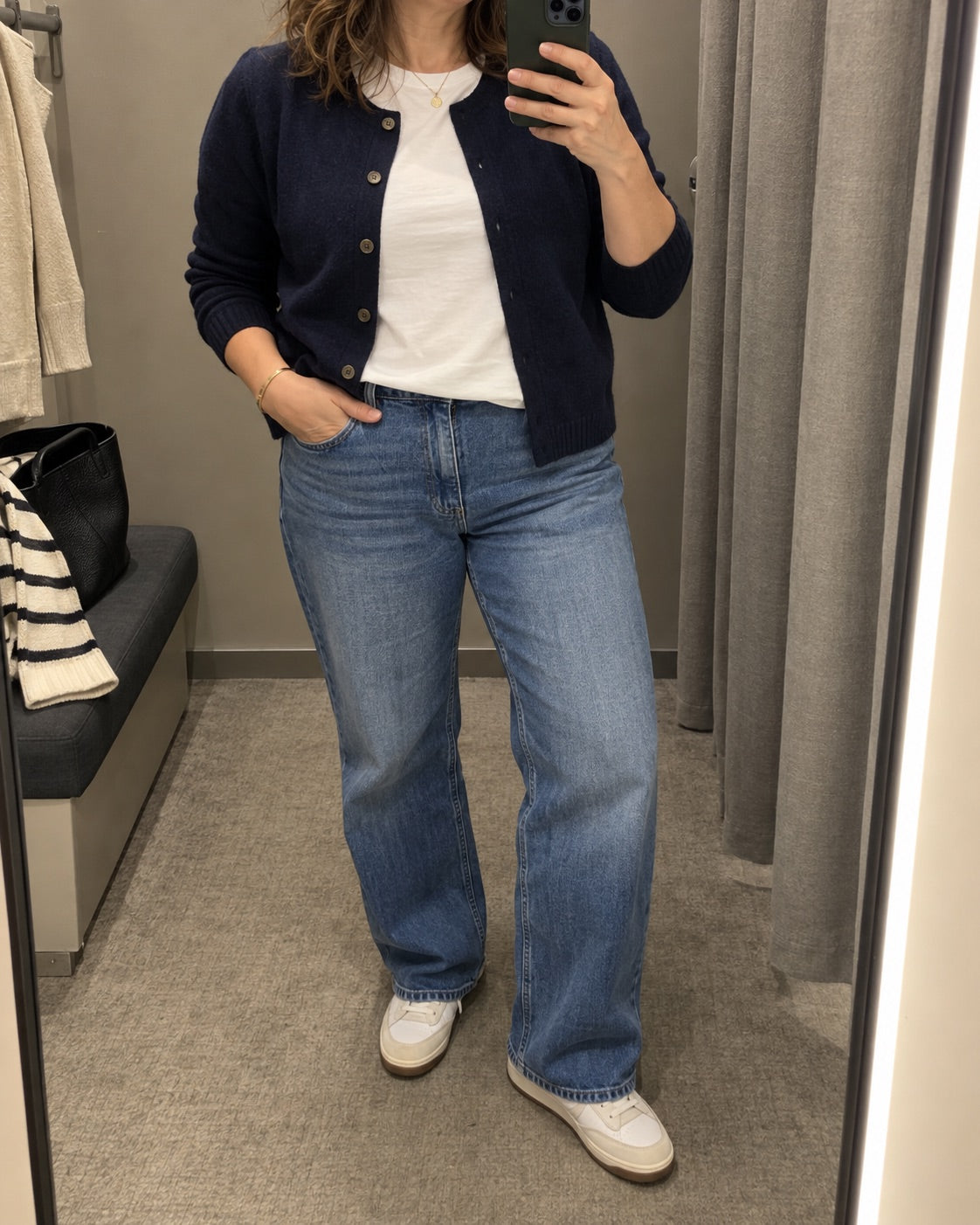 Woman wearing a navy cardigan and relaxed jeans in a changing-room mirror